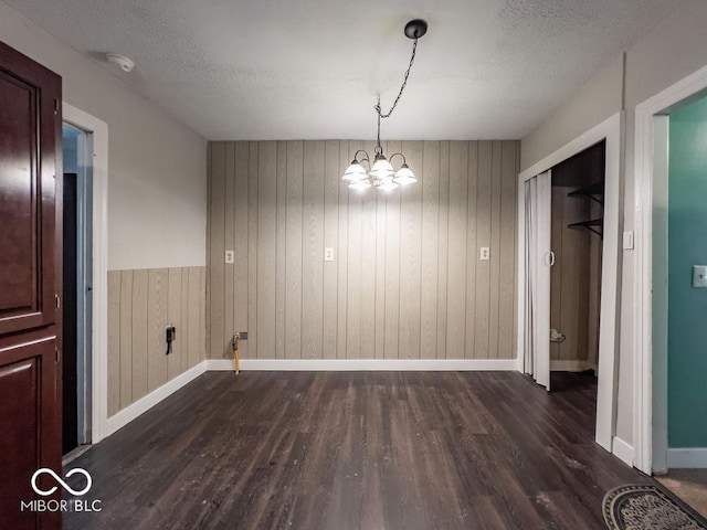 unfurnished dining area featuring an inviting chandelier, dark wood-type flooring, and a textured ceiling