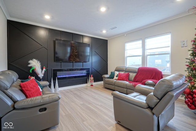 living room featuring a large fireplace, crown molding, and light hardwood / wood-style flooring