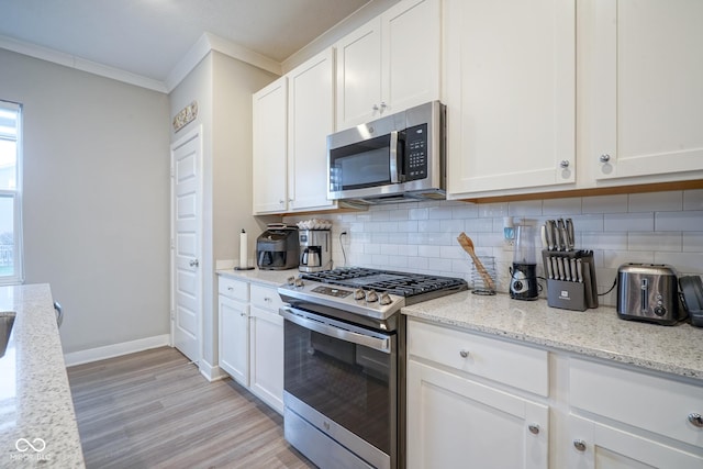 kitchen with light stone countertops, appliances with stainless steel finishes, tasteful backsplash, light hardwood / wood-style flooring, and white cabinets