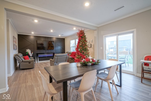 dining room with plenty of natural light, a fireplace, light wood-type flooring, and ornamental molding