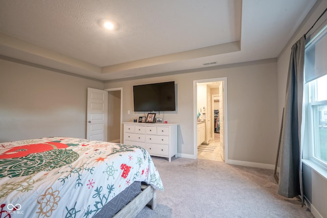 carpeted bedroom with a textured ceiling, a tray ceiling, and ensuite bath