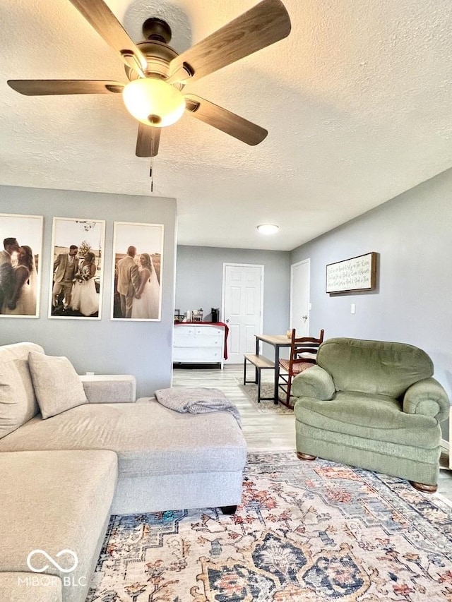 living room featuring ceiling fan, light hardwood / wood-style floors, and a textured ceiling