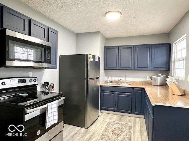 kitchen featuring appliances with stainless steel finishes, a textured ceiling, sink, blue cabinetry, and light hardwood / wood-style flooring