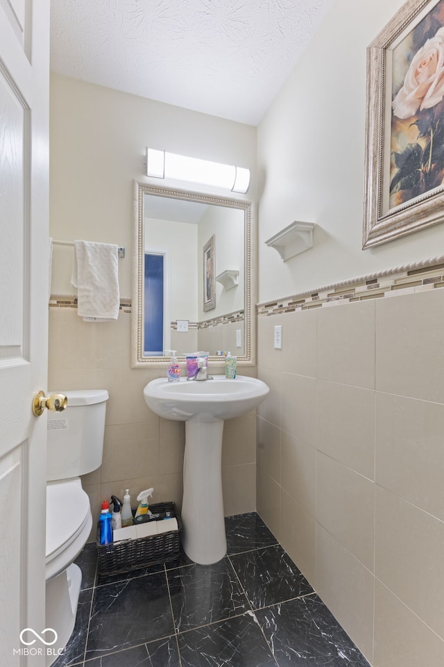 bathroom with a textured ceiling, toilet, and tile walls