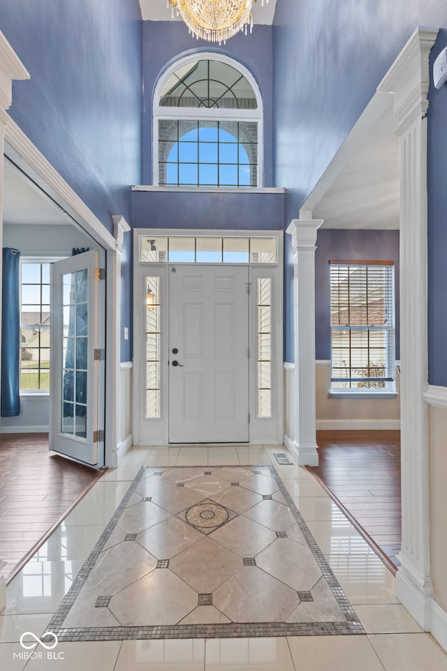 tiled entrance foyer with a high ceiling, ornate columns, and a notable chandelier