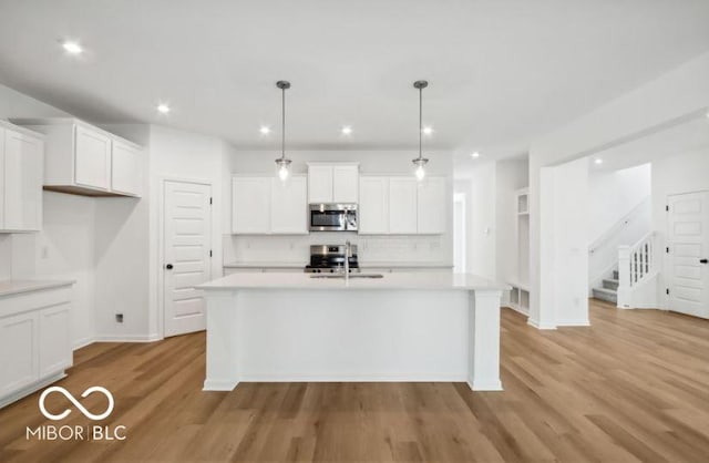 kitchen with stainless steel appliances, a center island with sink, white cabinets, light hardwood / wood-style floors, and hanging light fixtures