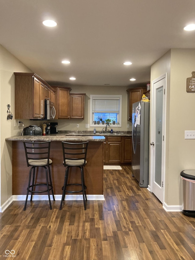 kitchen featuring a kitchen bar, appliances with stainless steel finishes, dark hardwood / wood-style floors, and kitchen peninsula