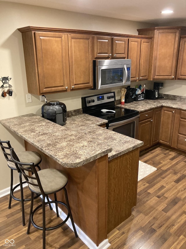 kitchen featuring kitchen peninsula, stainless steel appliances, light stone counters, and dark hardwood / wood-style floors