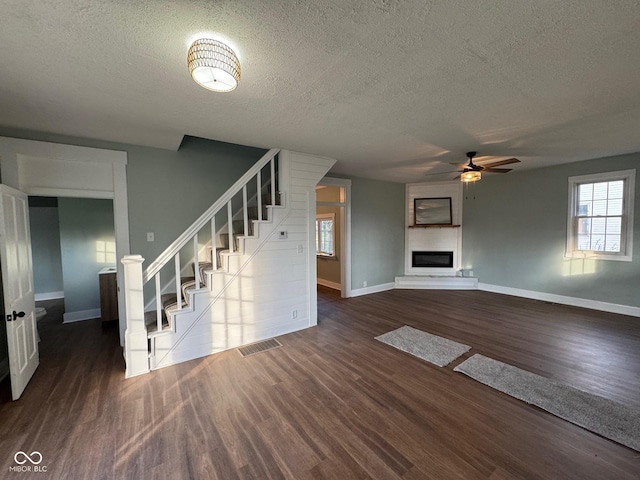 unfurnished living room featuring a textured ceiling, ceiling fan, a large fireplace, and dark hardwood / wood-style floors