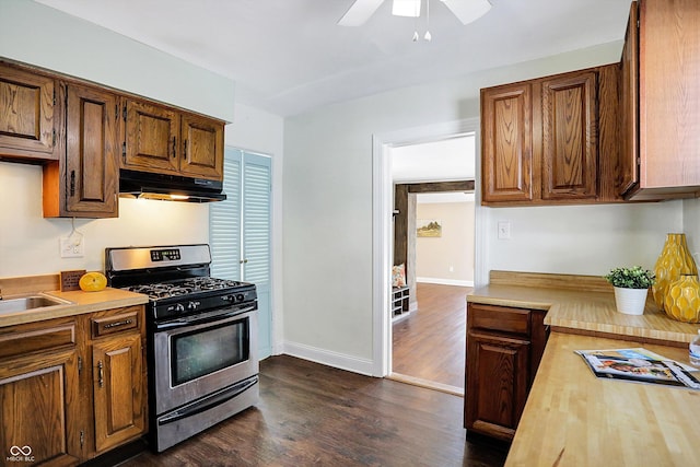 kitchen featuring dark wood-type flooring, stainless steel gas range oven, ceiling fan, and wood counters