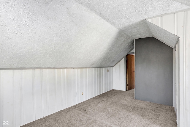 additional living space with a textured ceiling, vaulted ceiling, and carpet flooring