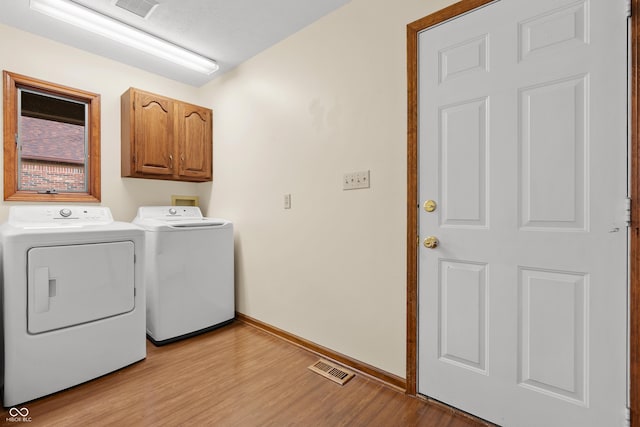 laundry room featuring cabinets, washing machine and dryer, and light hardwood / wood-style floors