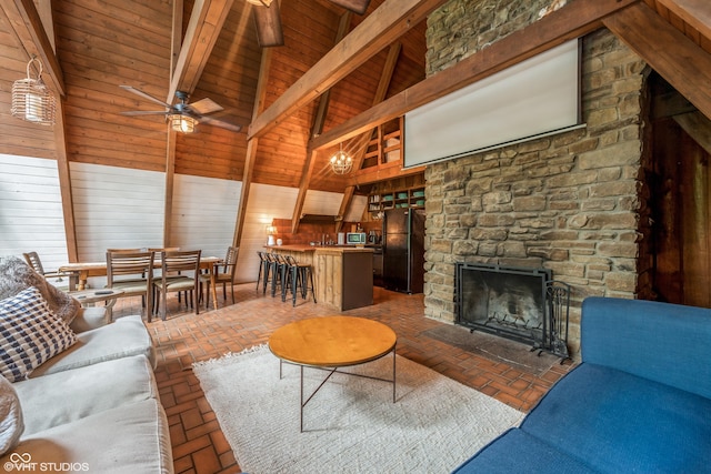 living room featuring ceiling fan, a stone fireplace, beamed ceiling, high vaulted ceiling, and wooden walls