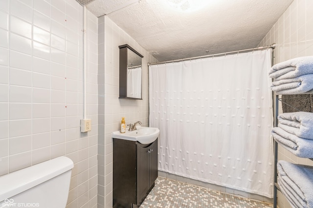 bathroom featuring a textured ceiling, vanity, tile walls, tile patterned flooring, and toilet