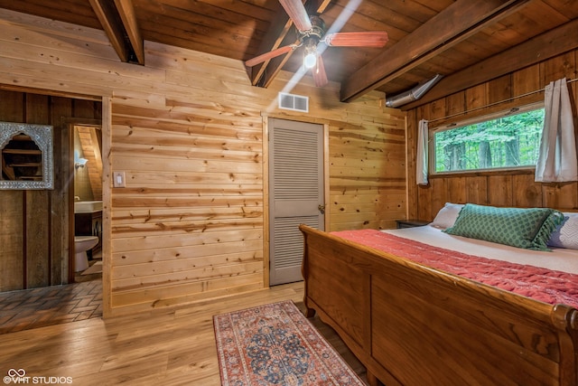 bedroom with wood walls, ensuite bath, light hardwood / wood-style flooring, ceiling fan, and beam ceiling