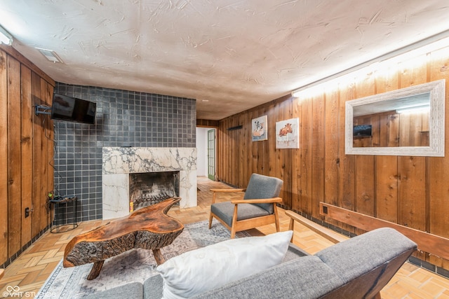 living room with a tiled fireplace, wooden walls, light parquet floors, and tile walls