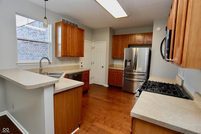 kitchen featuring sink, dark hardwood / wood-style floors, kitchen peninsula, pendant lighting, and appliances with stainless steel finishes