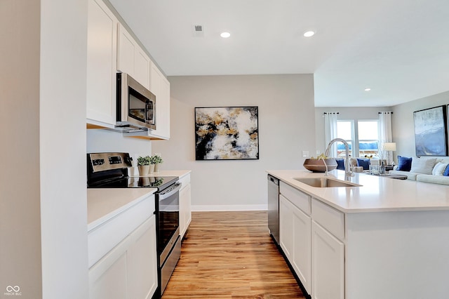 kitchen featuring appliances with stainless steel finishes, sink, light hardwood / wood-style flooring, white cabinetry, and an island with sink