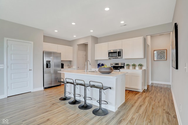 kitchen featuring white cabinets, light hardwood / wood-style floors, a kitchen island with sink, and appliances with stainless steel finishes