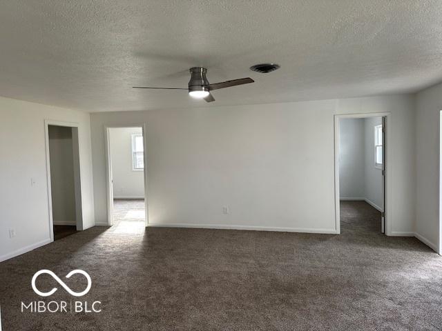 empty room featuring a healthy amount of sunlight, a textured ceiling, and dark carpet