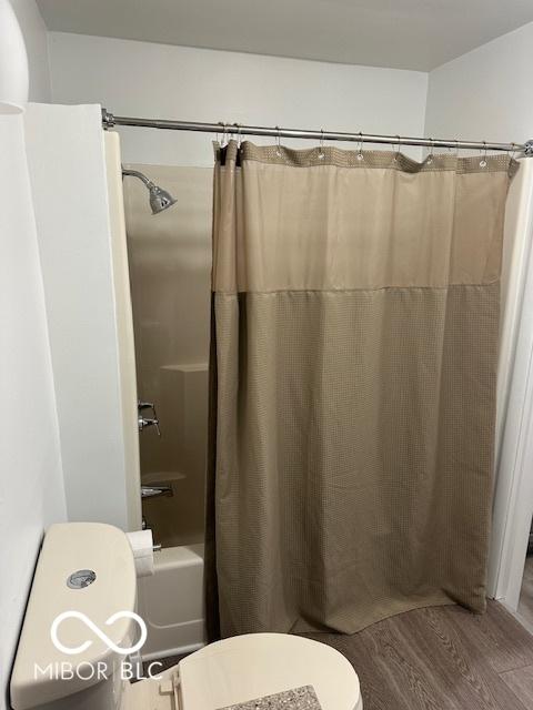 bathroom featuring hardwood / wood-style floors, toilet, and shower / bathtub combination with curtain