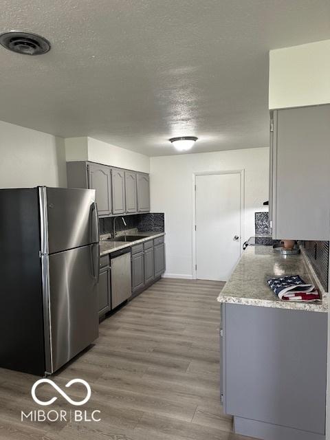 kitchen featuring gray cabinetry, sink, hardwood / wood-style flooring, a textured ceiling, and appliances with stainless steel finishes