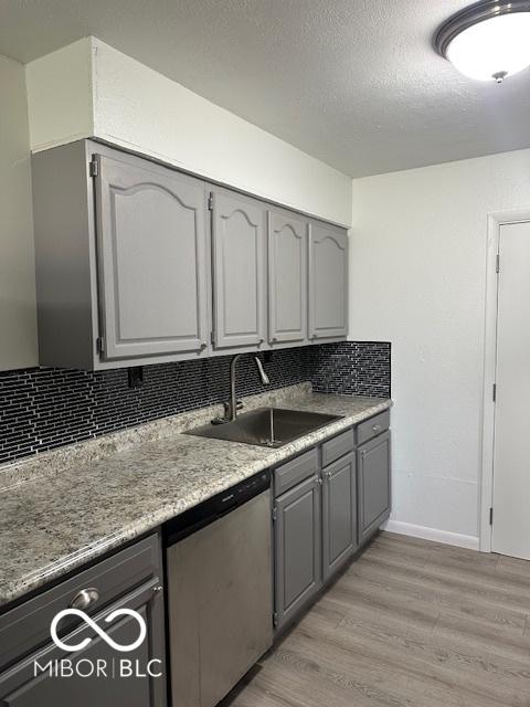 kitchen with gray cabinetry, dishwasher, backsplash, sink, and light wood-type flooring