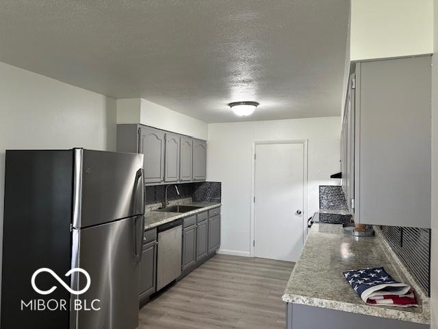 kitchen featuring appliances with stainless steel finishes, gray cabinetry, a textured ceiling, sink, and light hardwood / wood-style flooring