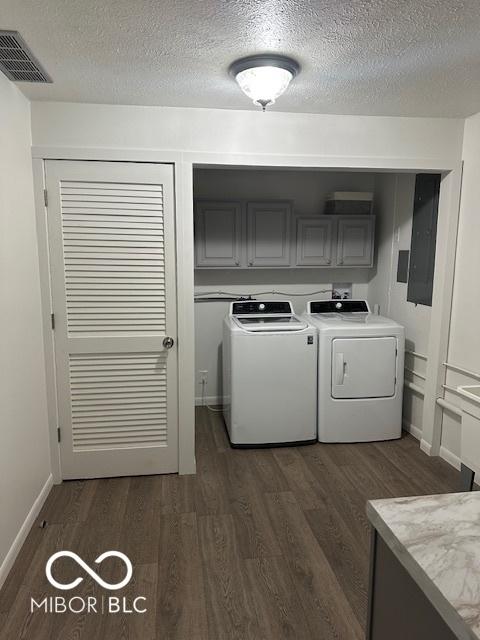 washroom featuring cabinets, washing machine and dryer, dark hardwood / wood-style floors, electric panel, and a textured ceiling