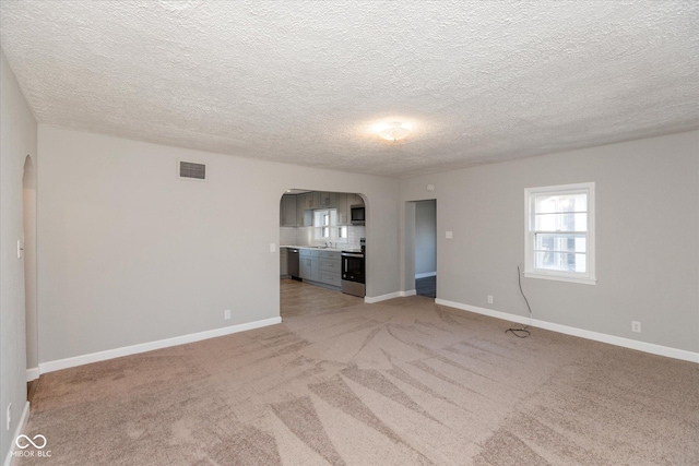 unfurnished living room featuring sink, light colored carpet, and a textured ceiling