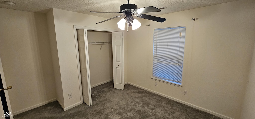 unfurnished bedroom with ceiling fan, a closet, a textured ceiling, and dark colored carpet