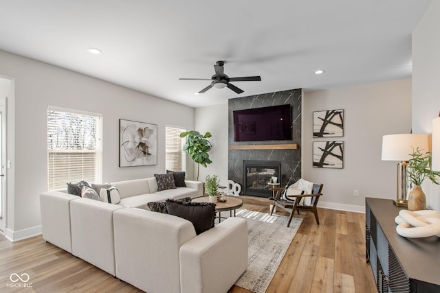 living room with a high end fireplace, light hardwood / wood-style floors, and ceiling fan