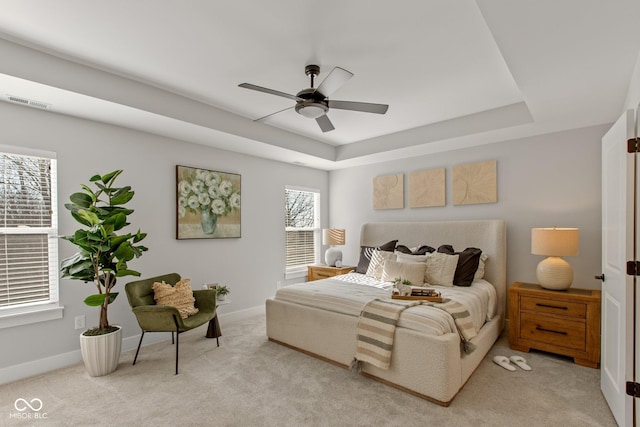 bedroom featuring a raised ceiling, light colored carpet, and ceiling fan