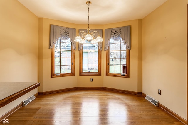 unfurnished dining area with wood-type flooring, an inviting chandelier, and a healthy amount of sunlight