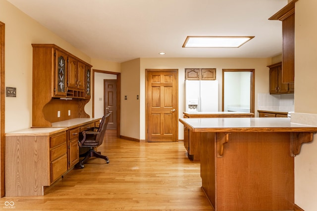 kitchen featuring white refrigerator with ice dispenser, kitchen peninsula, light hardwood / wood-style floors, a breakfast bar, and built in desk