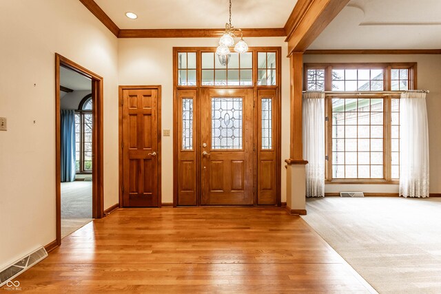 entrance foyer featuring light wood-type flooring, crown molding, and an inviting chandelier