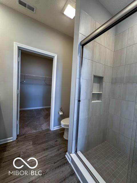 bathroom with hardwood / wood-style floors, a shower with shower door, and toilet