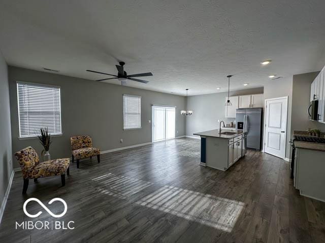 kitchen with stainless steel appliances, dark hardwood / wood-style floors, an island with sink, decorative light fixtures, and ceiling fan with notable chandelier