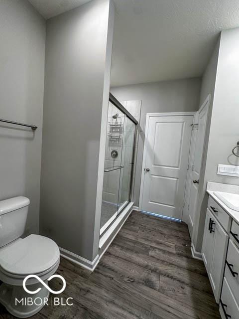 bathroom featuring hardwood / wood-style floors, vanity, a shower with door, and toilet