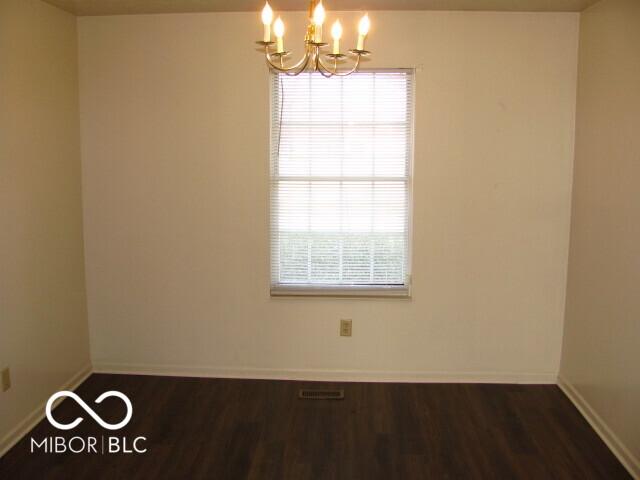 spare room featuring a notable chandelier and dark wood-type flooring