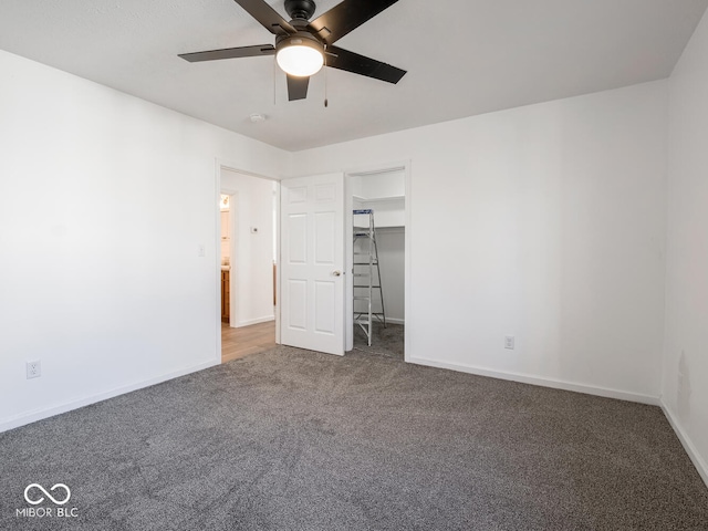 unfurnished bedroom with a walk in closet, a closet, dark carpet, and ceiling fan