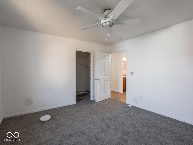 unfurnished bedroom with dark carpet, ceiling fan, a spacious closet, a textured ceiling, and a closet