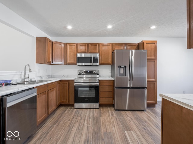 kitchen with light stone countertops, appliances with stainless steel finishes, a textured ceiling, sink, and hardwood / wood-style floors