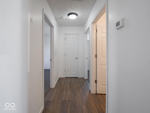 corridor with a textured ceiling and dark hardwood / wood-style floors