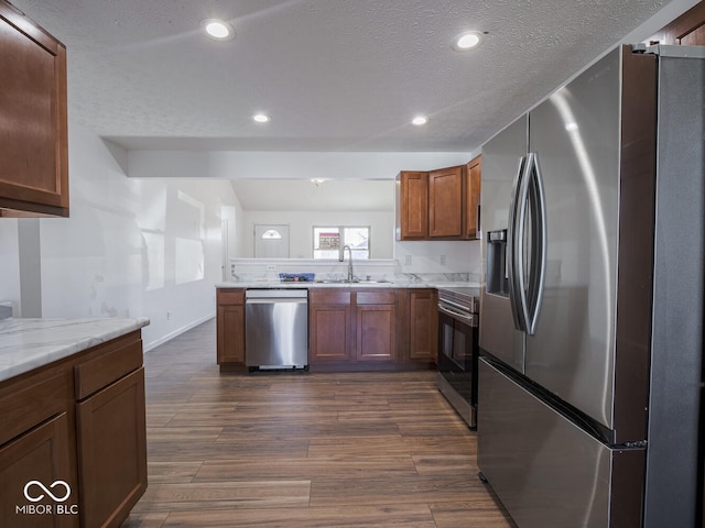 kitchen with dark wood-type flooring, sink, a textured ceiling, appliances with stainless steel finishes, and light stone counters