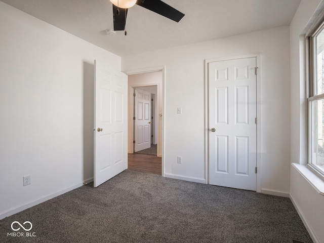 unfurnished bedroom featuring dark colored carpet, ceiling fan, and multiple windows