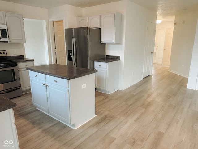 kitchen with stainless steel appliances, a center island, white cabinets, and light hardwood / wood-style flooring