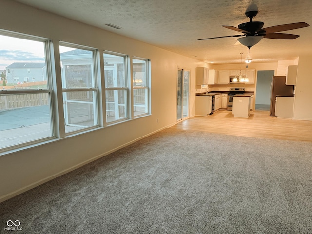 unfurnished living room with ceiling fan, light colored carpet, and a textured ceiling