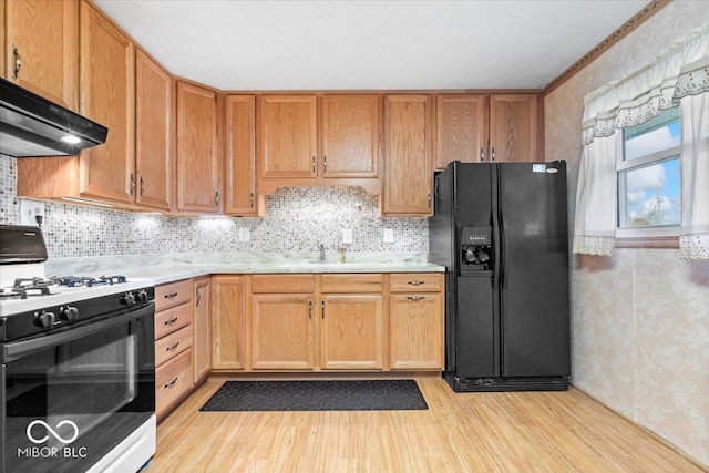 kitchen featuring sink, white gas range oven, tasteful backsplash, black fridge, and light wood-type flooring