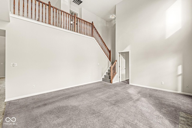 unfurnished living room with baseboards, visible vents, stairway, a high ceiling, and carpet floors